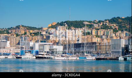 Gênes, Italie - 28 juin 2025 : rangées de voiliers amarrés le long du quai à Gênes, Italie, avec des bâtiments colorés à flanc de colline s'élevant au-dessus du port sur un cercle Banque D'Images