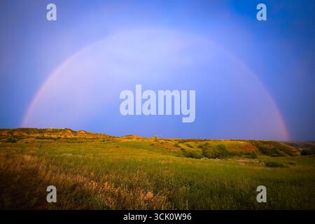 Une image à couper le souffle capture les couleurs vives d'un magnifique coucher de soleil peignant le ciel, avec un magnifique arc-en-ciel qui forme un arc sur de vastes prairies ouvertes Banque D'Images