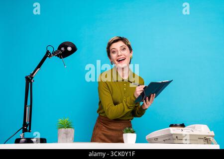 Jeune femme responsable travaillant avec plaisir avec des documents dans un cadre de bureau élégant avec des éléments rétro sur bleu Banque D'Images