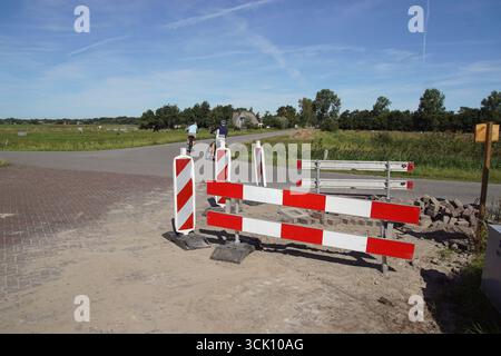 Travaux routiers dans la rue avec briques et panneaux de signalisation. Poteaux d'avertissement et barrières routières rayés rouges et blancs. Paysage de pâturages hollandais. Septembre, Banque D'Images