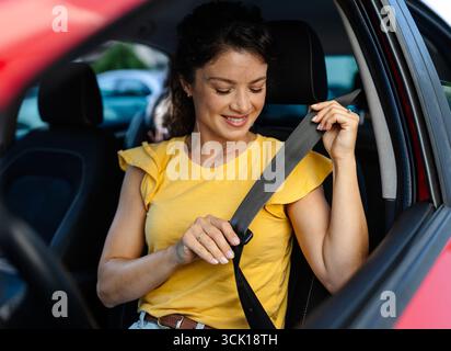 Femme attachant sa ceinture de sécurité alors qu'elle était assise dans une voiture. Un enfant est visible sur la banquette arrière, ajoutant à l'atmosphère joyeuse Banque D'Images