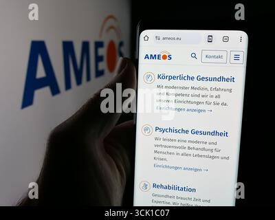 Dans cette illustration photo, une personne tient un téléphone portable avec la page Web de la société suisse de soins de santé AMEOS Holding AG sur l'écran devant le logo. Banque D'Images
