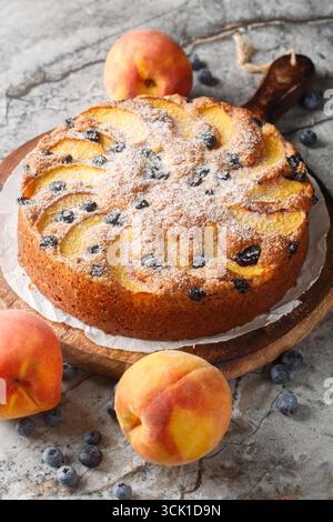 Gâteau éponge de myrtille de pêche saupoudré de sucre en poudre gros plan sur une planche de bois sur la table. Vertical Banque D'Images