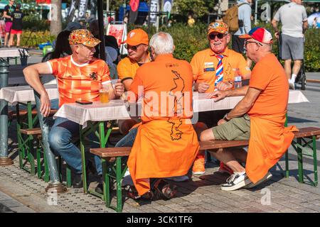 Groupe de fans de football néerlandais vêtus de vêtements orange, assis ensemble et buvant à une table en plein air dans un espace public avant le match Banque D'Images