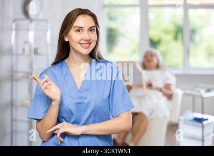 Femme médecin cosmétologue debout avec la femme regardant miroir derrière dans le bureau des médecins. Banque D'Images