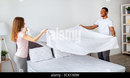 Couple multiracial gai faisant lit le matin, s'amuser à la maison Banque D'Images