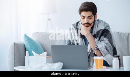 Malade arabe homme employé souffrant de virus mais besoin de travailler, de travailler sur ordinateur portable et de prendre des pilules pour la grippe. Banque D'Images