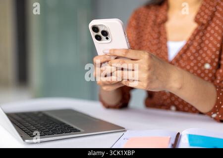 Femme d'affaires tient smartphone dans les mains, en utilisant le téléphone portable et l'ordinateur portable au lieu de travail, naviguant sur Internet sur téléphone portable, travaillant au bureau avec bloc-notes et ordinateur portable Banque D'Images