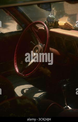 Gros plan du volant rouge vif et de l'intérieur rouge de la voiture rétro avec bâton de vitesse noir. Mini boule disco sur rétroviseur, intérieur baigné de soleil Banque D'Images