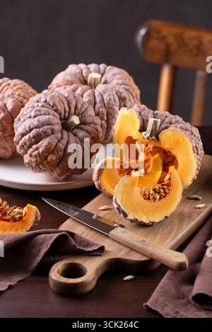 Courge Futsu noire entière et coupée avec chair orange vif et coins sur Une table de cuisine prête pour la cuisson Banque D'Images