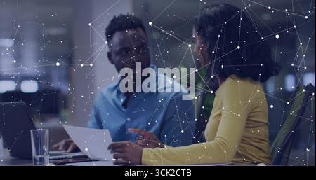 Femme jaune tenant le document guidant l'homme tapant sur ordinateur portable au bureau, avec superposition de réseau Banque D'Images