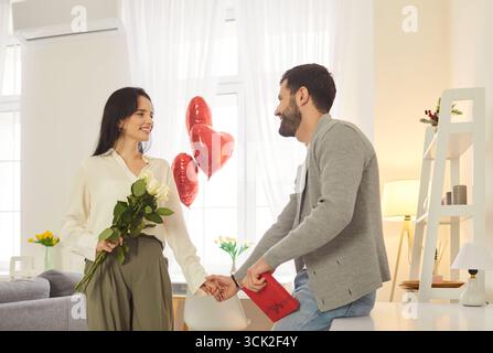 Jeune couple joyeux et souriant debout, se tenant par la main et célébrant la Saint-Valentin à la maison. Banque D'Images