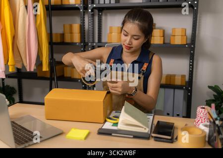 Jeune femme entrepreneure scellant soigneusement le paquet avec du ruban adhésif, préparant les commandes de marchandises, gérant l'expédition et la livraison pour son succès en ligne Banque D'Images