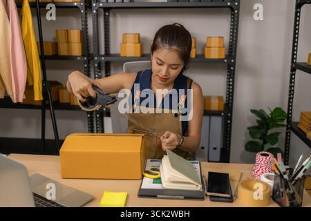 Jeune femme entrepreneure scellant soigneusement le paquet avec du ruban adhésif, préparant les commandes de marchandises, gérant l'expédition et la livraison pour son succès en ligne Banque D'Images