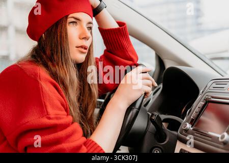 Femme conduisant une voiture. La jeune femme au béret rouge regarde soigneusement par la fenêtre de la voiture. Banque D'Images