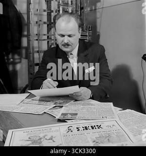 Portrait d'un rédacteur en chef ou d'un militant du parti travaillant sur un numéro du journal satirique mural 'Yozhik' (Hedgehog) dans un bureau de communication à Sloviansk, RSS d'Ukraine, en février 1975. La photographie d'archive capture un homme avec une barre de ruban sur sa veste éditant des documents pour le journal étalé sur son bureau. Cette scène montre les « coulisses » du travail idéologique soviétique local, où les activistes sociaux ont utilisé la « critique camarade » pour combattre les lacunes du collectif ouvrier pendant l'ère de stagnation Banque D'Images