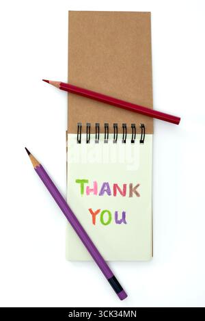 Une note de remerciement est affichée bien en évidence sur un bloc-notes en spirale entouré de crayons de couleur. La note présente un lettrage lumineux et coloré contre un su Banque D'Images