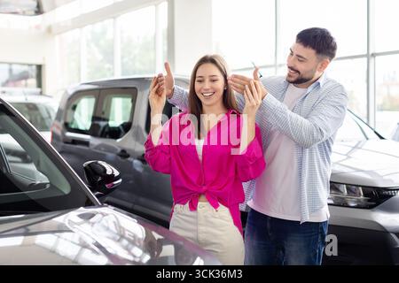 Homme aimant faisant la surprise à la femme avec l'achat de voiture, couvrant ses yeux Banque D'Images