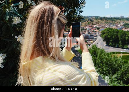 Jeune femme prend des photos de smartphone de paysage pittoresque dans une ville pendant une journée ensoleillée Banque D'Images