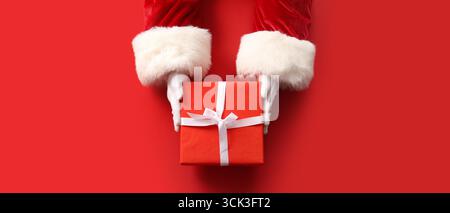 Mains du Père Noël avec cadeau de Noël sur fond rouge, vue de dessus Banque D'Images
