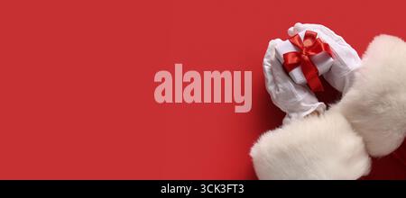 Mains du Père Noël avec cadeau de Noël sur fond rouge avec espace pour le texte Banque D'Images