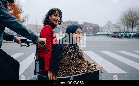 Deux amis sourient et profitent d'une balade amusante dans la ville, capturant une expérience de plein air et joyeuse tout en conduisant une voiturette à vélo à travers un envir urbain animé Banque D'Images