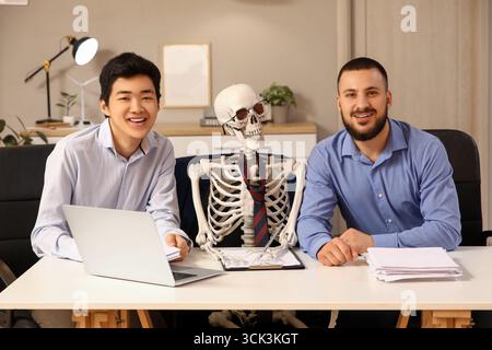 Collègues masculins avec squelette humain à table dans le bureau Banque D'Images