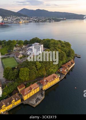 Vue aérienne des bâtiments jaunes vibrants nichés le long du front de mer serein, contrastant avec les arbres verdoyants de la péninsule, Bergen, Vestland, Norvège. Banque D'Images