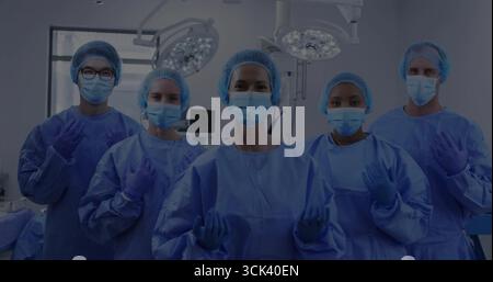 Debout cinq membres du personnel médical ajustant les gants dans la salle d'opération, portant des blouses bleues et des casquettes de cheveux Banque D'Images