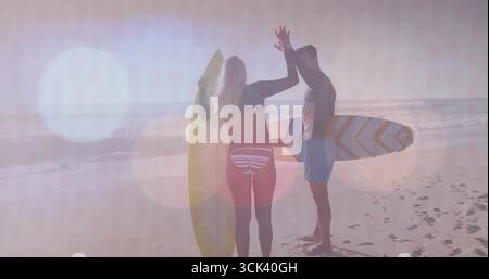 Surfeurs adultes de haut niveau portant des combinaisons sur le sable de plage au lever du soleil, avec planches de surf, empreintes de pas Banque D'Images