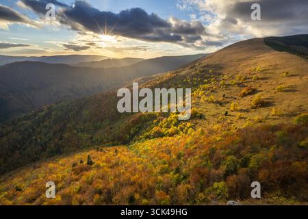 Les couleurs de l'automne enflamment les collines ondulantes tandis que le soleil éclate à travers les nuages spectaculaires sur les sereines montagnes Velka Fatra, Staré Hory, Banskobystrický kraj, Slovaquie. Banque D'Images