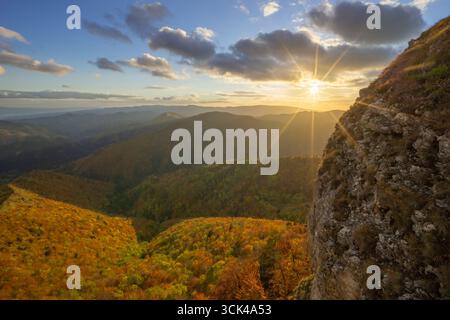 Vue du soleil éclatant à l'horizon, projetant une lumière dorée sur les forêts aux couleurs automnales et les falaises rocheuses, le rocher Majerova Skala, Staré Hory, Banskobys Banque D'Images