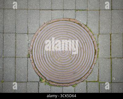 Couvercle rond de trou d'homme sur la rue pavée en pierre avec motif circulaire Banque D'Images