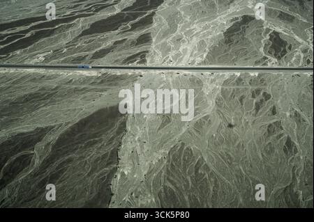 Camion bleu sur l'autoroute Panamericana sur traversant le plateau de Nazca, Pérou, avec des traces de rivières saisonnières Banque D'Images