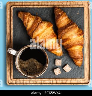 Une scène de petit déjeuner confortable avec deux croissants et une tasse de café noir avec des cubes de sucre sur un plateau en bois. Banque D'Images