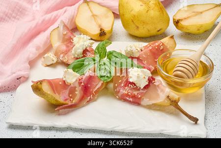 Tranche de poire enveloppée dans du prosciutto avec du fromage et des graines de sésame sur un tableau blanc, vue de dessus Banque D'Images