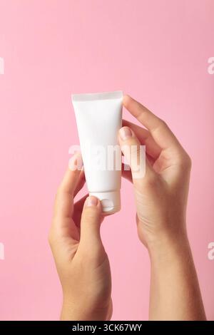Main tenant le tube en plastique blanc vierge sur fond rose. Vue de dessus Banque D'Images