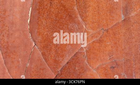 Un gros plan de la surface texturée de roche brun rougeâtre présentant des motifs naturels et des fissures. Banque D'Images