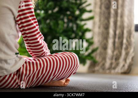 Garçon habillé comme un elfe assis sur le sol regardant le sapin de Noël Banque D'Images
