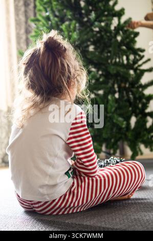 Garçon habillé comme un elfe assis sur le sol regardant le sapin de Noël Banque D'Images