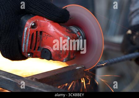 Meuleuse d'angle coupe barre d'armature, étincelles volantes. Meuleuse d'angle avec disque métallique et sans boîtier, violation de sécurité. Gros plan des mains gantées avec broyeur Banque D'Images
