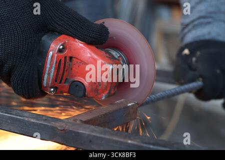 Meuleuse d'angle coupe barre d'armature, étincelles volantes. Meuleuse d'angle avec disque métallique et sans boîtier, violation de sécurité. Gros plan des mains gantées avec broyeur Banque D'Images