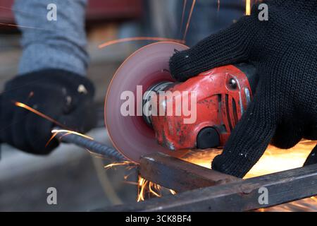 Meuleuse d'angle coupe barre d'armature, étincelles volantes. Meuleuse d'angle avec disque métallique et sans boîtier, violation de sécurité. Gros plan des mains gantées avec broyeur Banque D'Images