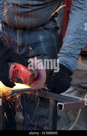 Meuleuse d'angle coupe barre d'armature, étincelles volantes. Meuleuse d'angle avec disque métallique et sans boîtier, violation de sécurité. Gros plan des mains gantées avec broyeur Banque D'Images