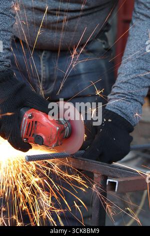 Meuleuse d'angle coupe barre d'armature, étincelles volantes. Meuleuse d'angle avec disque métallique et sans boîtier, violation de sécurité. Gros plan des mains gantées avec broyeur Banque D'Images