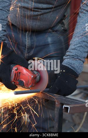 Meuleuse d'angle coupe barre d'armature, étincelles volantes. Meuleuse d'angle avec disque métallique et sans boîtier, violation de sécurité. Gros plan des mains gantées avec broyeur Banque D'Images