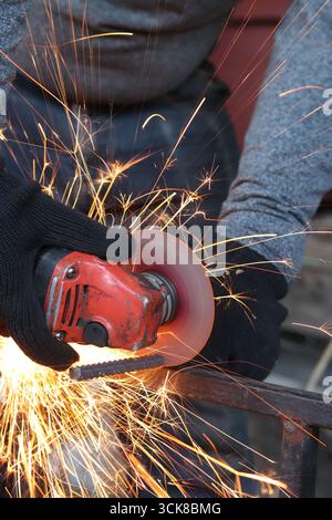 Meuleuse d'angle coupe barre d'armature, étincelles volantes. Meuleuse d'angle avec disque métallique et sans boîtier, violation de sécurité. Gros plan des mains gantées avec broyeur Banque D'Images