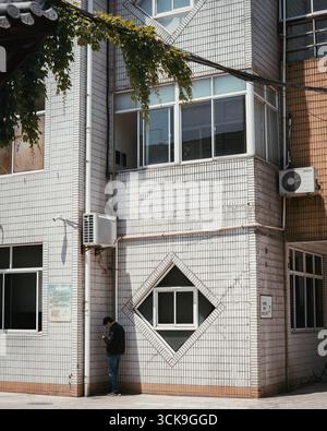 Homme debout près d'un bâtiment carrelé avec un design de fenêtre géométrique unique dans une zone urbaine Banque D'Images