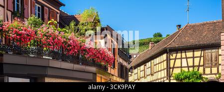 Charmante scène de rue dans un village pittoresque de Ribeauville, avec des fleurs colorées sur des balcons, des maisons traditionnelles à colombages, et un clair Banque D'Images