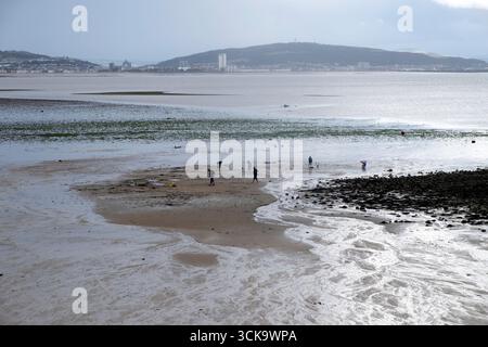Paysage marin vue des gens sur la plage à marée basse regardant à travers la baie de Swansea au centre-ville et les collines de Mumbles South Wales UK KATHY DEWITT Banque D'Images